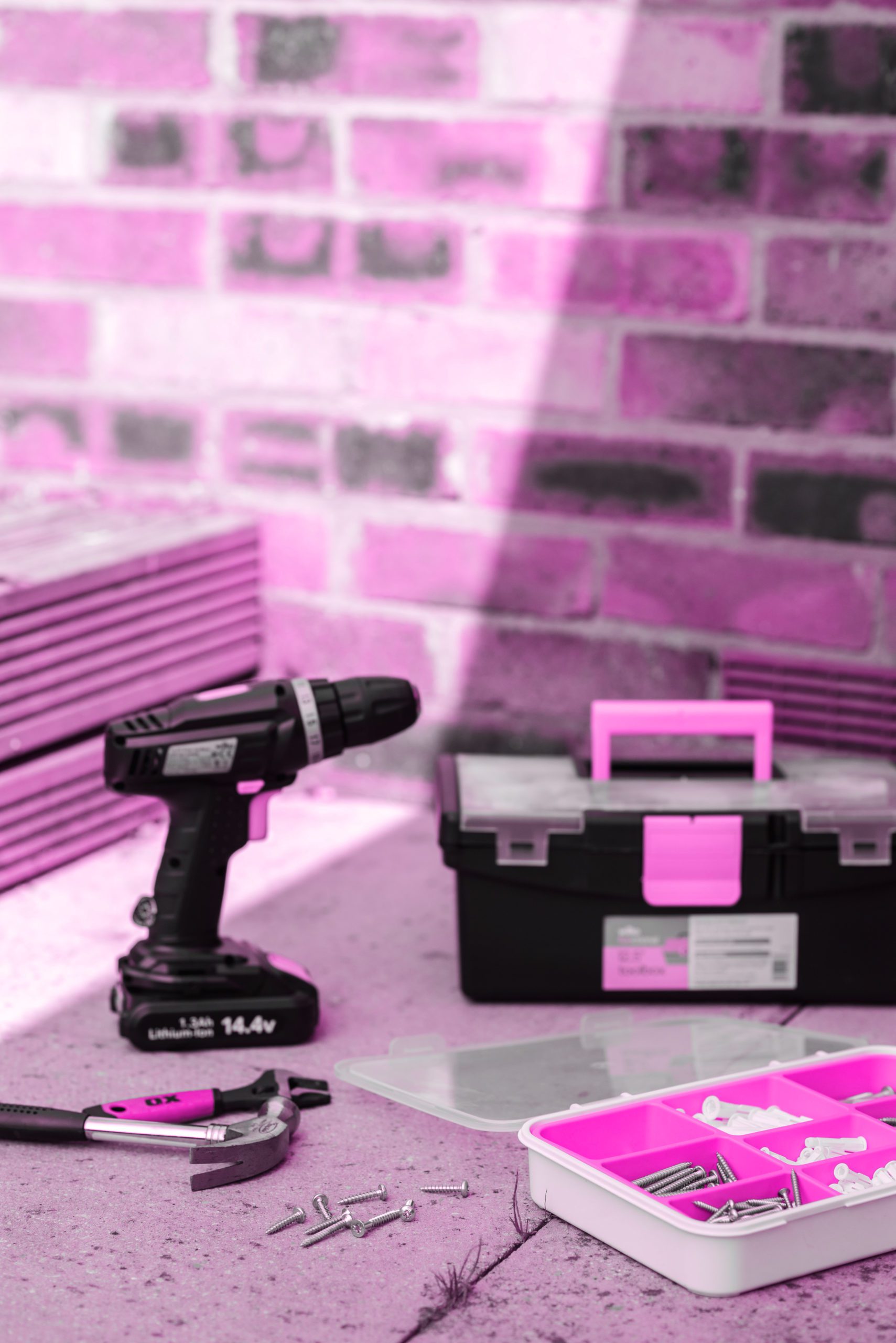 Pink filtered image of a drill, toolbox and other tools near a brick wall - female electrician moncton