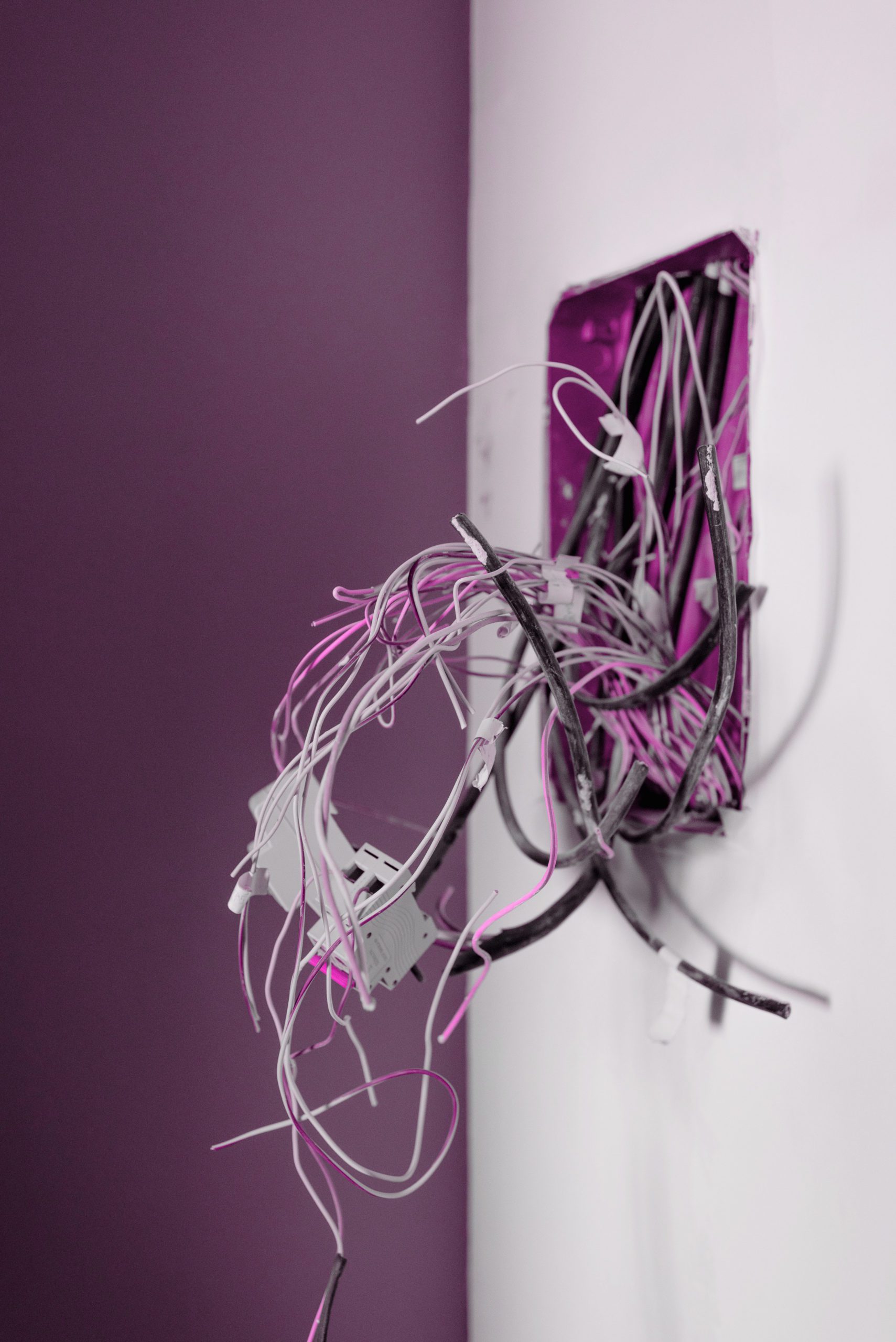 Pink filtered image of a white wall with untidy wire bundles pulled out - wire tidying Twisted Electric